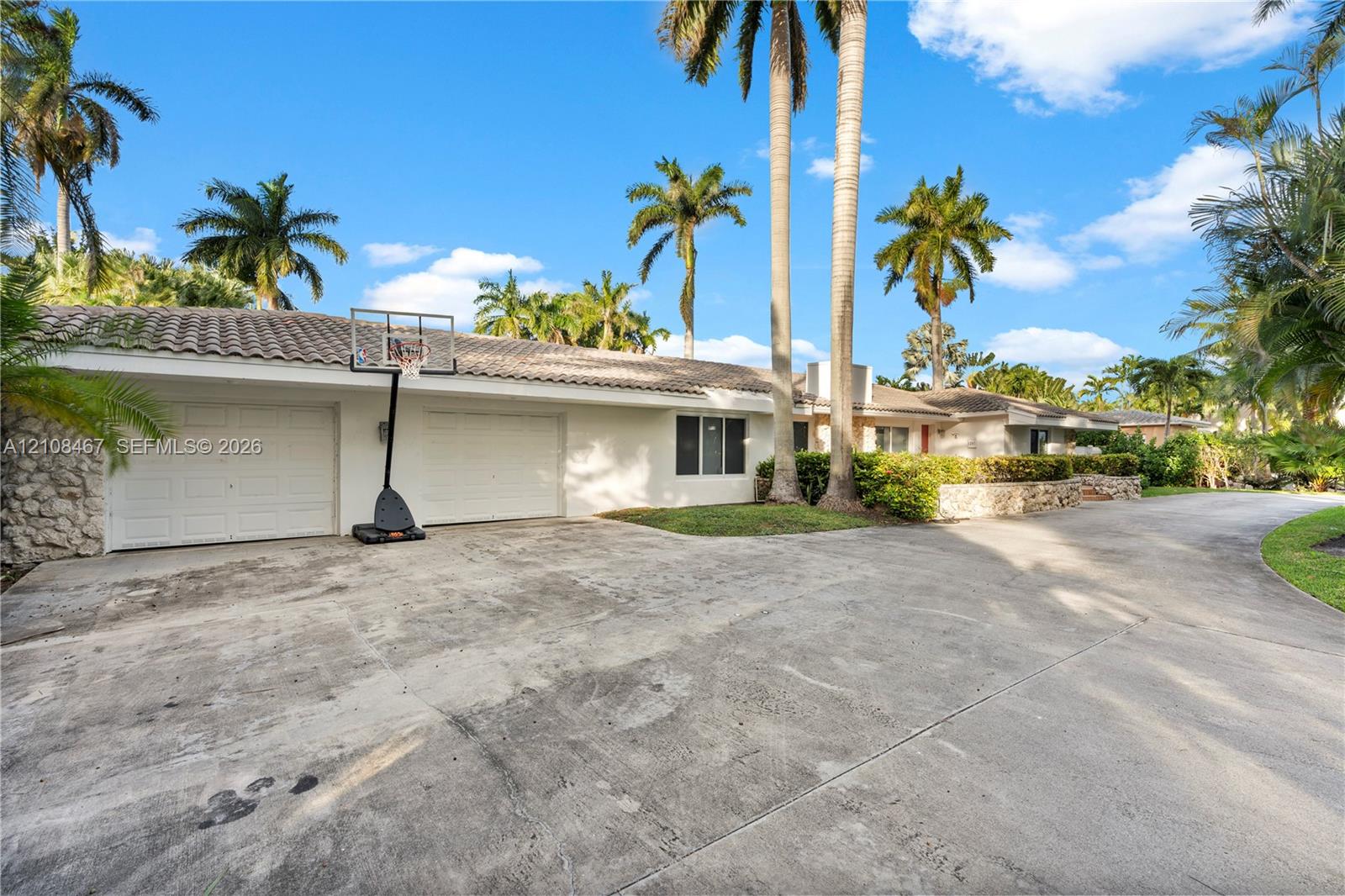Single-story exterior featuring a concrete driveway, dual-car garage, stone veneer siding, and a tile roof, complemented by established palm trees