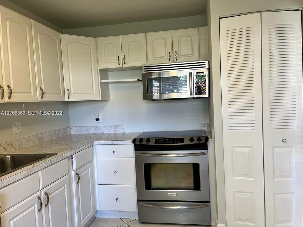 Kitchen featuring white cabinetry, stone-finish countertops, stainless steel appliances, and pantry for extra storage