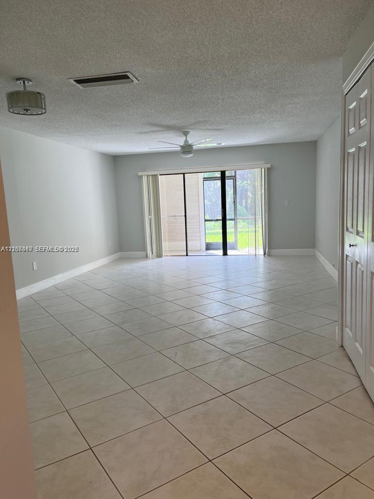 Spacious room featuring tile flooring, a ceiling fan, a drum-style pendant light, and a sliding glass door to access a screened lanai with conservation views
