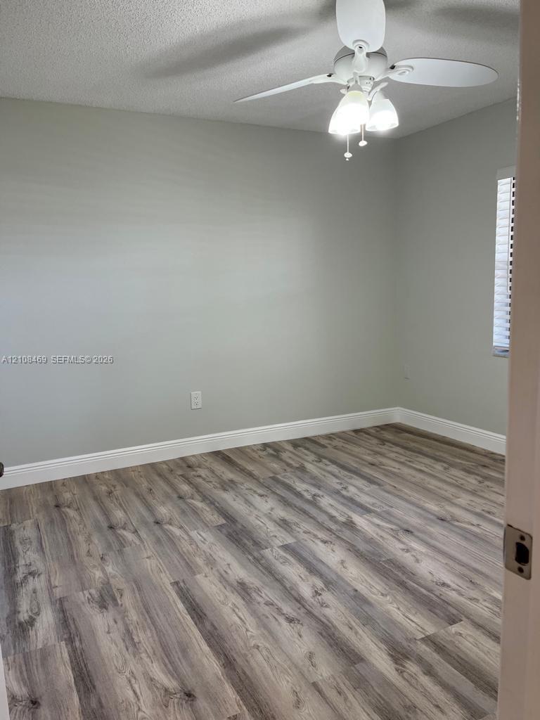Wood-finish flooring, neutral wall tones, white ceiling fan with integrated three-light fixture, and window blinds