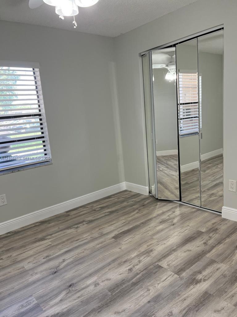 Wood-finish flooring, mirrored sliding closet doors, horizontal slat window blinds, and a ceiling-mounted light fixture