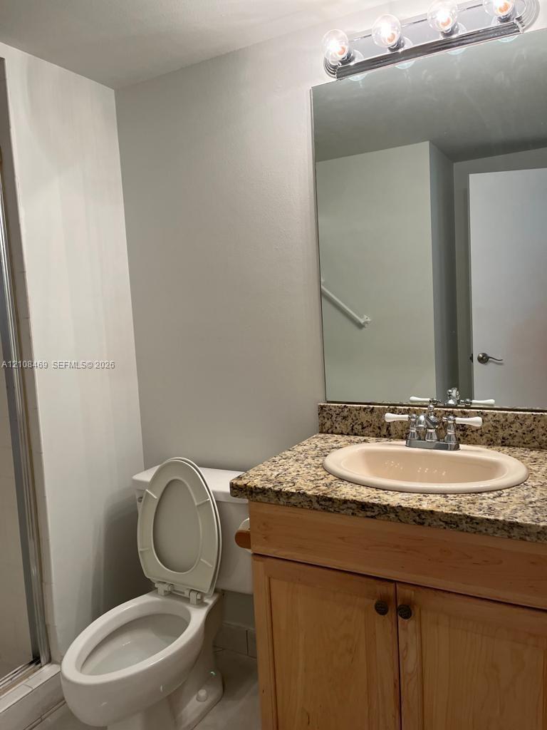 Bathroom with shower, vanity featuring a natural stone countertop, undermount sink, light wood cabinetry, and a multi-bulb vanity light fixture above a wall-mounted mirror