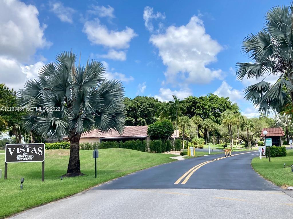 Paved entrance road featuring mature palm trees, manicured lawn.