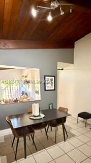 Vaulted wood-plank ceiling with exposed beam, ceramic tile flooring, and multi-light adjustable ceiling fixture