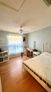 Bedroom featuring wood-finish flooring, diagonal paneled accent wall, ceiling fan with integrated lighting, and window with built-in rod