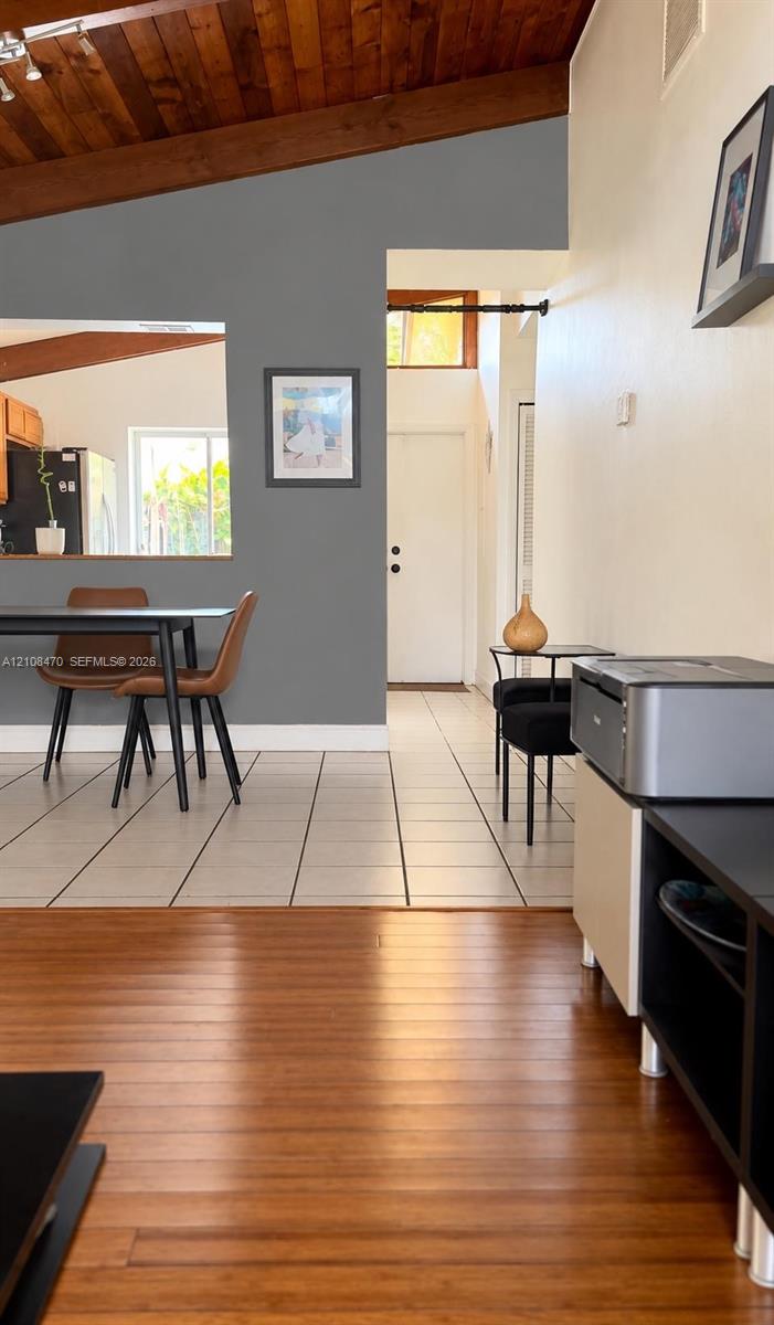 Vaulted wood-plank ceiling featuring exposed structural beams, tile flooring, and wood-finish flooring