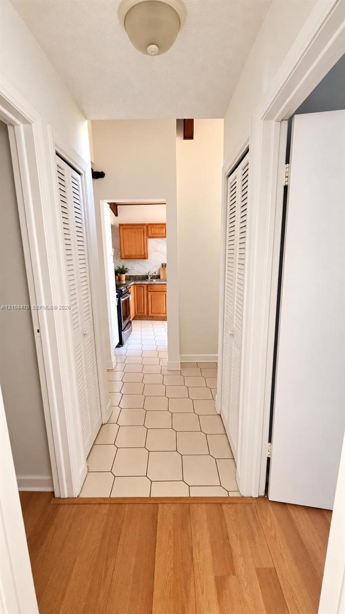 Hallway featuring wood-finish flooring, dual louvered-style closet doors, geometric tile flooring, and a flush-mount ceiling fixture