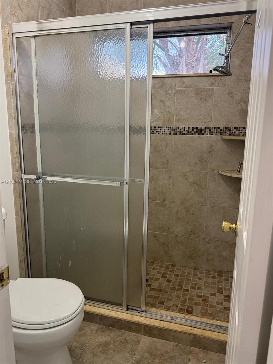 Walk-in shower featuring a sliding glass door, tile surround with decorative mosaic inlay, built-in shelving, and a small horizontal window