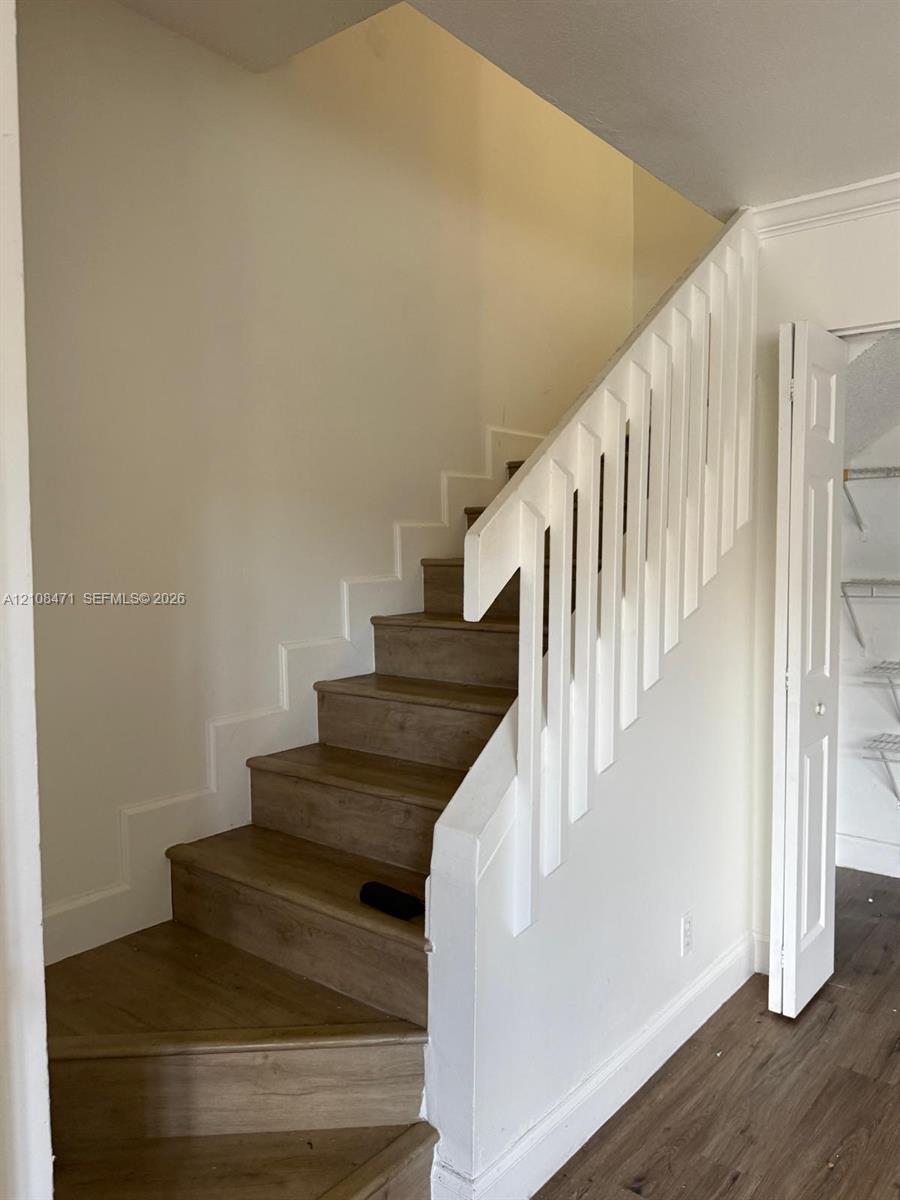 Staircase featuring wood-finish treads, a white handrail with vertical balusters, and a built-in closet with wire shelving