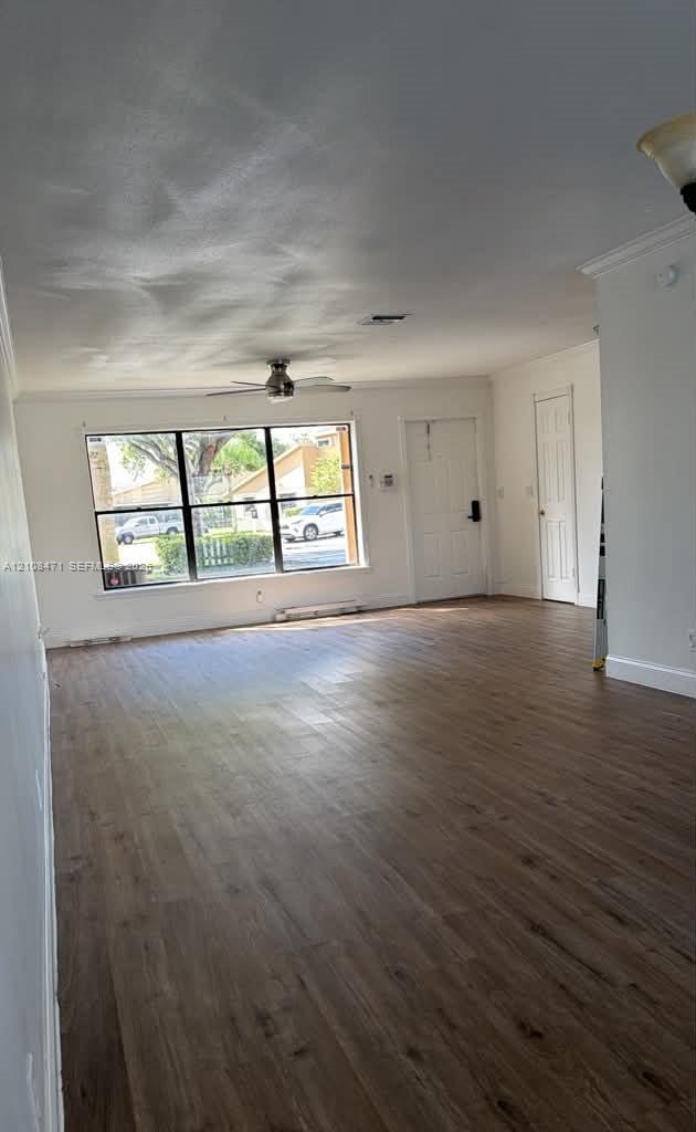 Open-concept interior featuring wood-finish flooring, a large picture window, a ceiling fan, and crown molding