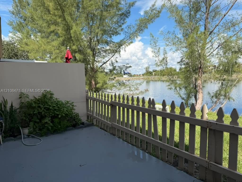 Concrete patio featuring a picket fence, mature trees, and water frontage