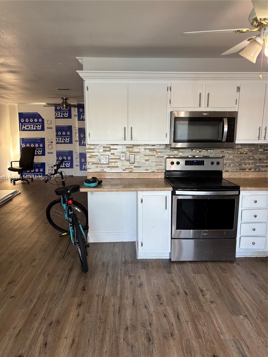 Kitchen featuring white cabinetry, wood-finish flooring, stainless steel appliances, and a glass-tile backsplash