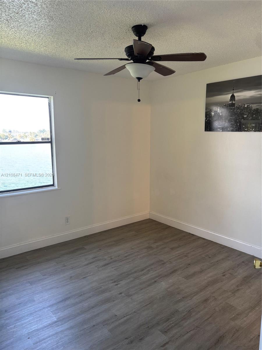 Room featuring wood-finish flooring, a ceiling fan with integrated lighting, and a window with water exposure
