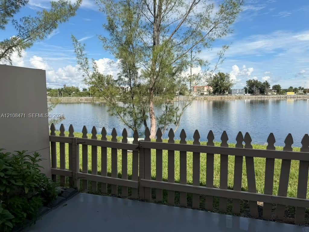 Concrete patio featuring a picket fence, manicured lawn, and water frontage Concrete patio featuring a picket fence, manicured lawn, and water frontage