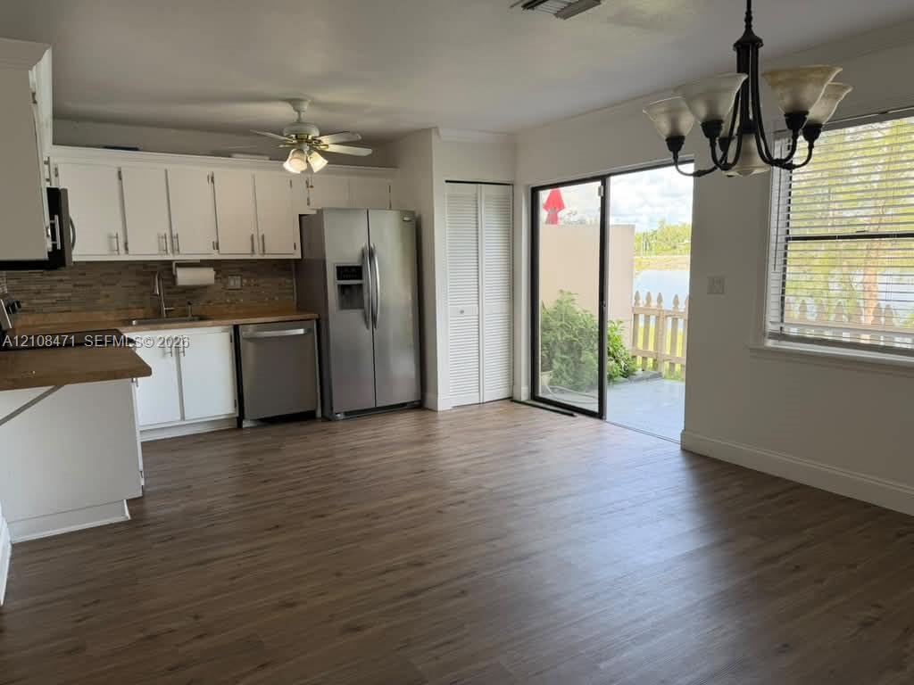 Kitchen featuring white shaker-style cabinetry, wood-finish flooring, stainless steel appliances, tiled backsplash, and sliding glass doors