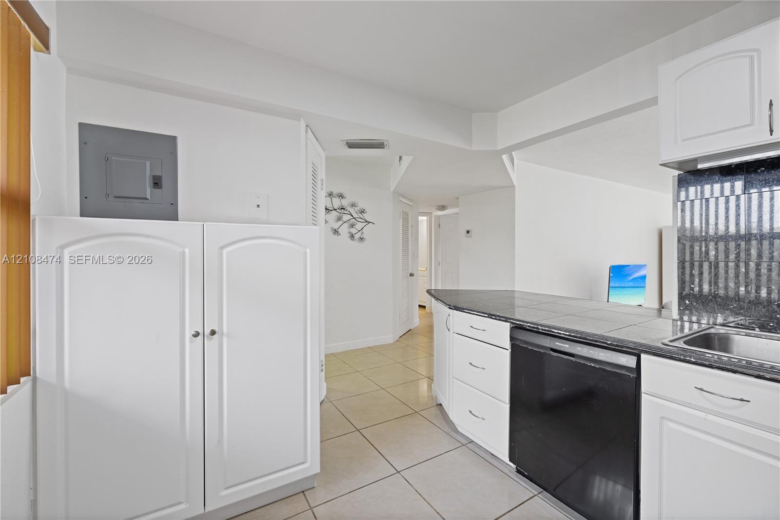 Kitchen featuring white shaker-style cabinetry, dark stone-finish countertops, tiled flooring, and a stainless steel built-in dishwasher