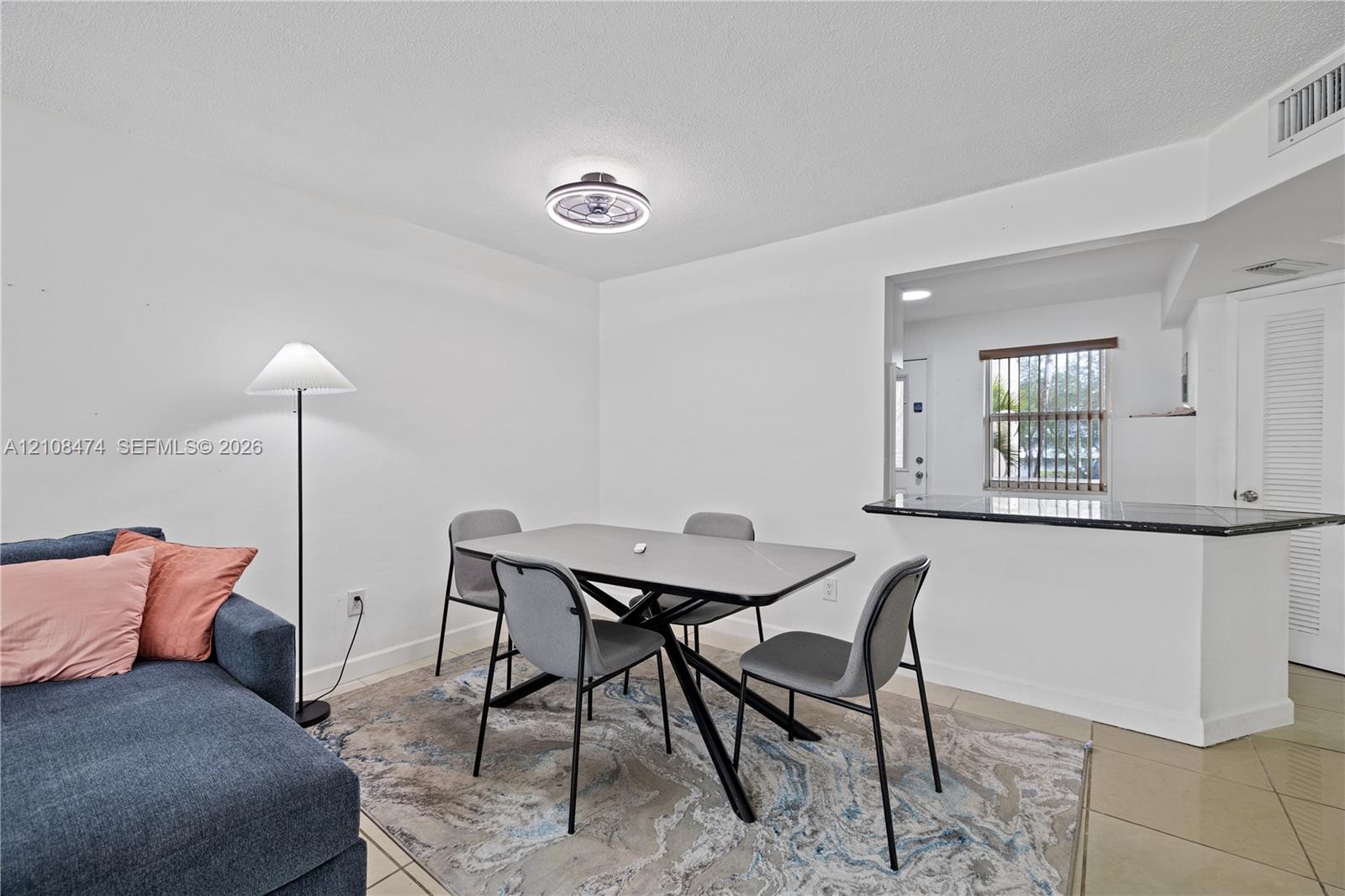 Open-concept interior featuring stone-surfaced pass-through counter, neutral tile flooring, and integrated ceiling-mounted light fixture