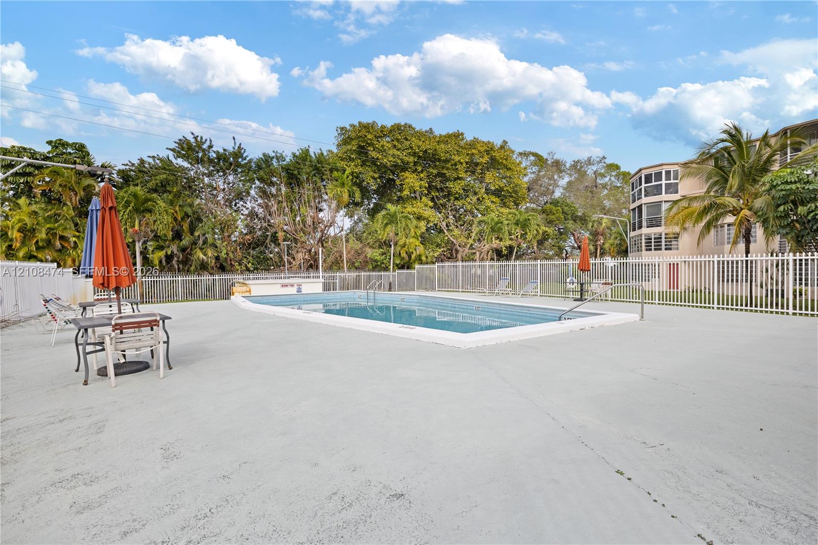 In-ground swimming pool featuring a concrete deck, perimeter fencing, and mature landscaping