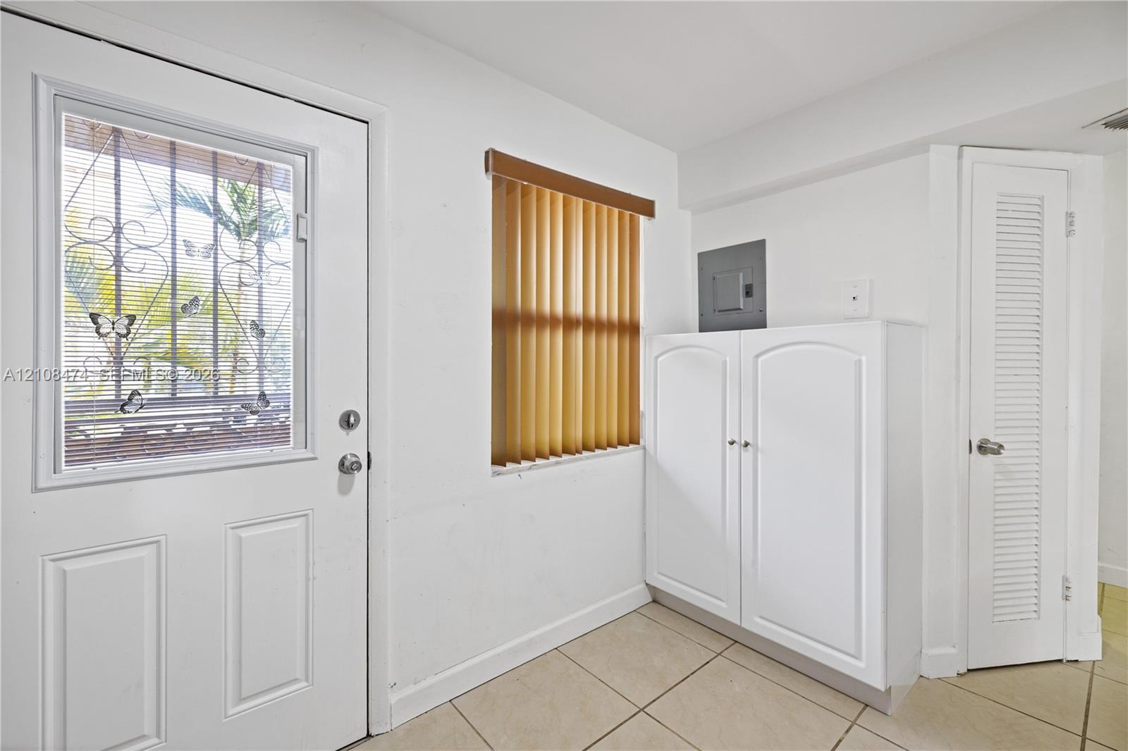 Exterior door with decorative security grating, tile flooring, built-in cabinetry, and louvered closet door