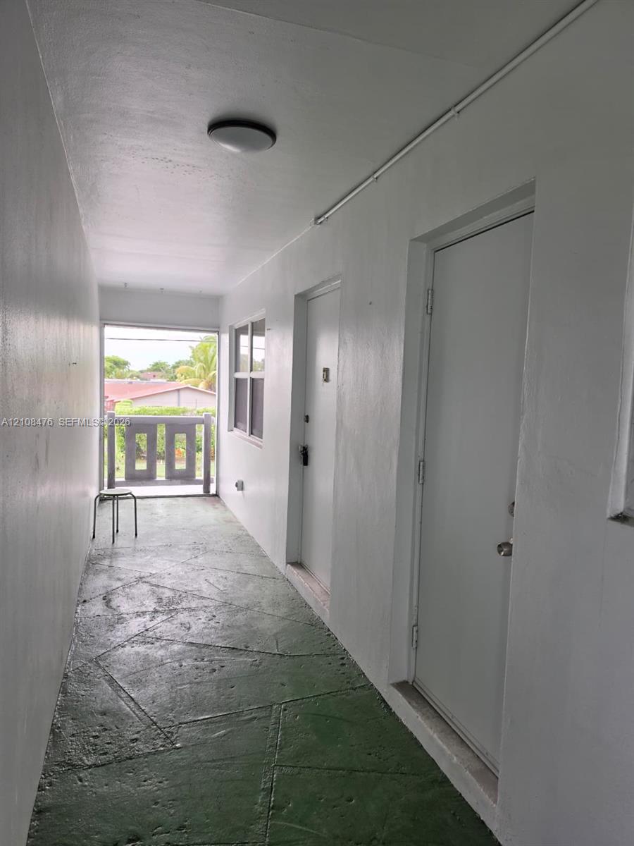 Covered exterior walkway featuring a painted concrete floor, solid-panel doors, flush-mount ceiling lighting, and a metal railing Covered exterior walkway featuring a painted concrete floor, solid-panel doors, flush-mount ceiling lighting, and a metal railing