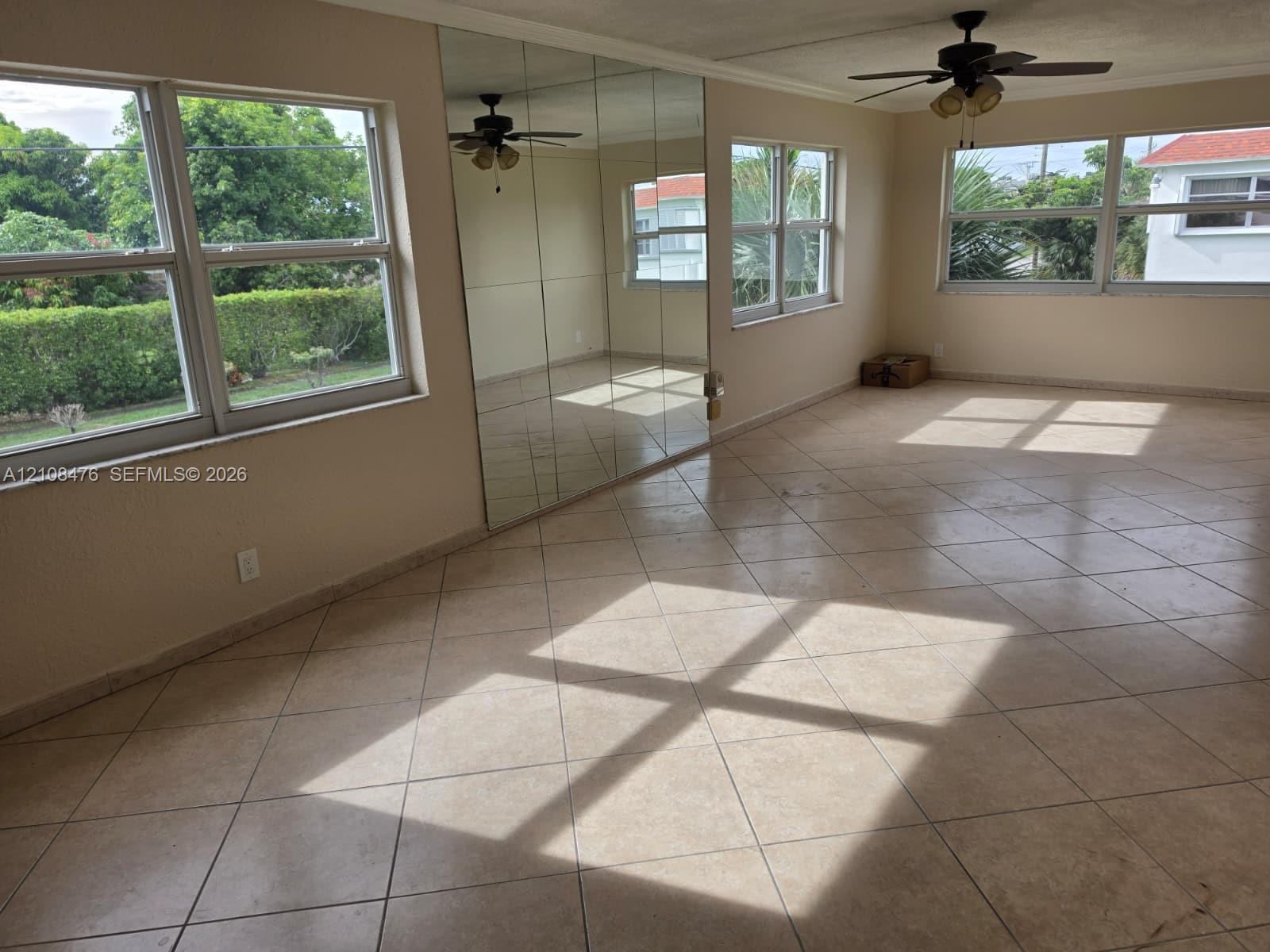 Large multi-pane window configuration, neutral ceramic tile flooring, floor-to-ceiling wall mirror, and dual ceiling-mounted fans Large multi-pane window configuration, neutral ceramic tile flooring, floor-to-ceiling wall mirror, and dual ceiling-mounted fans