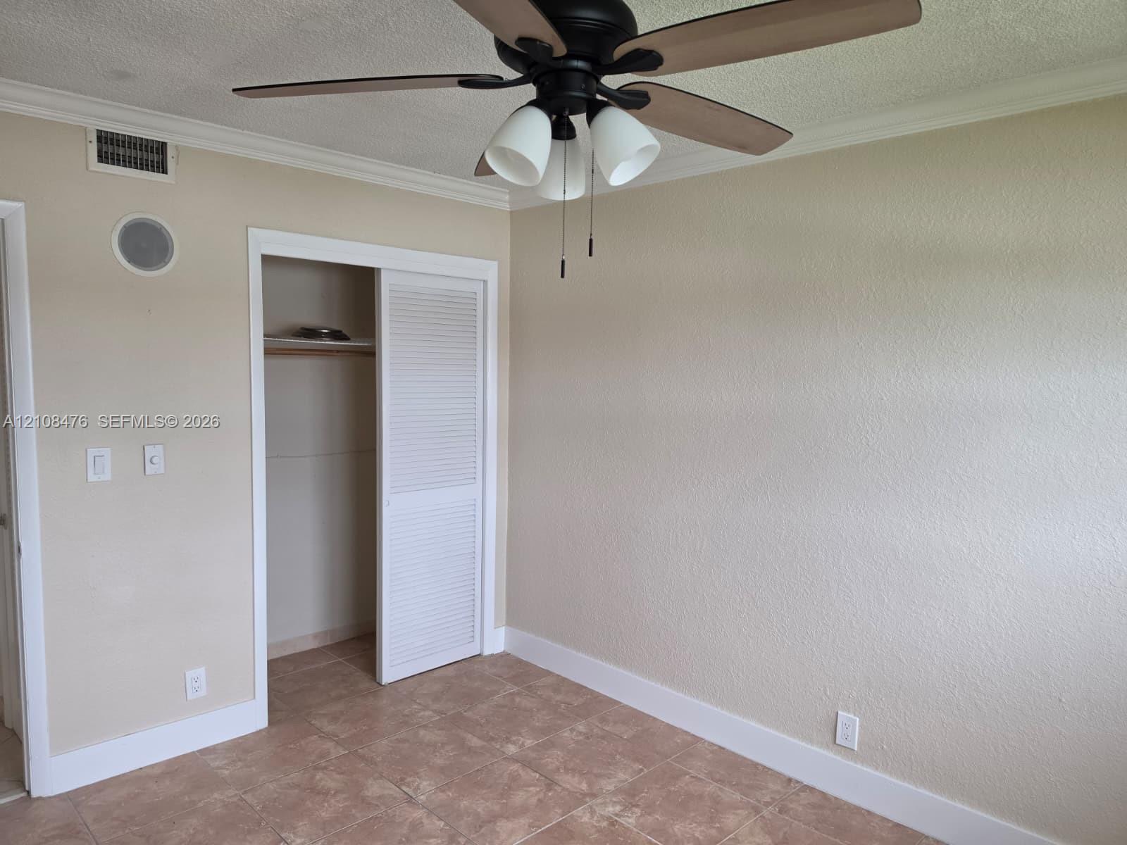 Room featuring neutral-toned wall paint, tile flooring, ceiling fan with integrated lighting, and a closet with louvered doors