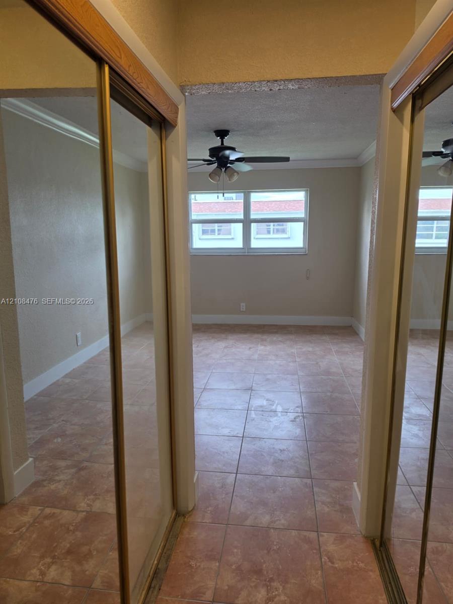 Tile flooring, dual mirrored sliding closet doors with wooden trim, and a ceiling fan with integrated lighting