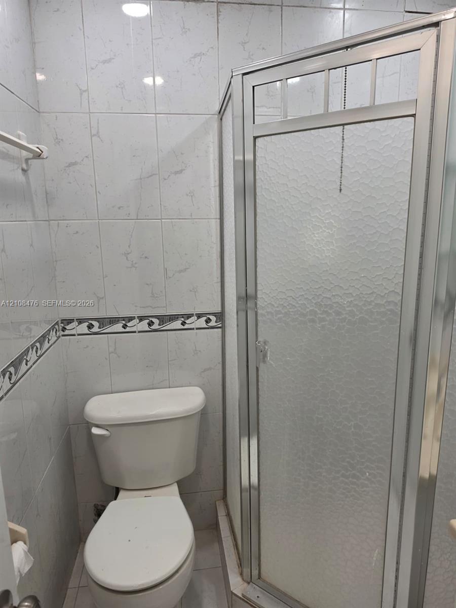 Bathroom featuring floor-to-ceiling ceramic tile, decorative accent trim, a corner shower enclosure with textured glass panels, and a standard-height toilet