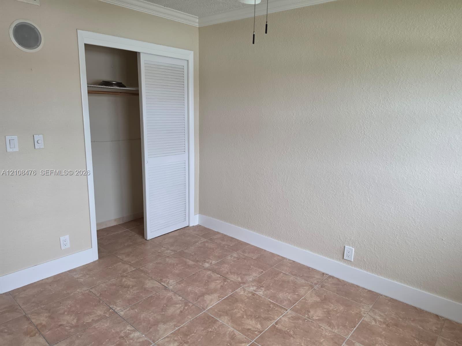 Neutral-toned walls with crown molding, ceramic tile flooring, and a closet featuring louvered sliding doors