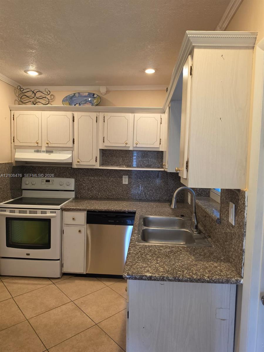 Kitchen featuring white cabinetry with crown molding, stone-patterned countertops, a full-height backsplash, stainless steel dual-basin sink with arched faucet, and ceramic tile flooring Kitchen featuring white cabinetry with crown molding, stone-patterned countertops, a full-height backsplash, stainless steel dual-basin sink with arched faucet, and ceramic tile flooring
