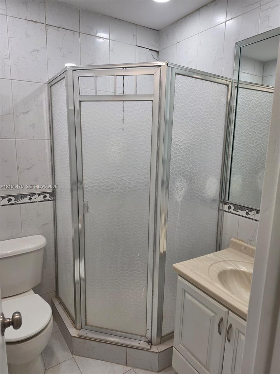 Corner shower stall with a metal-framed glass enclosure, vanity with a molded countertop and basin, ceramic tile wall finishes with decorative accents, and polished edge mirror Corner shower stall with a metal-framed glass enclosure, vanity with a molded countertop and basin, ceramic tile wall finishes with decorative accents, and polished edge mirror