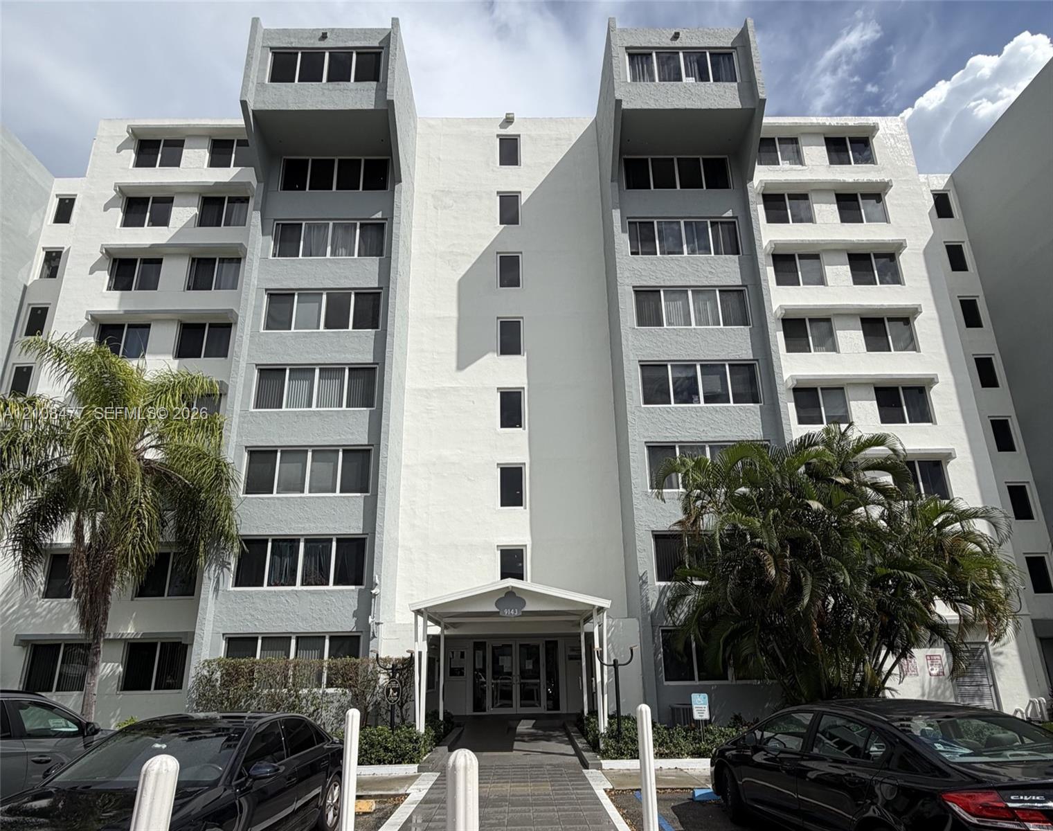 Multi-story exterior featuring a textured facade, structural roofline extensions, multiple rows of grid-pattern windows, and a covered building entrance