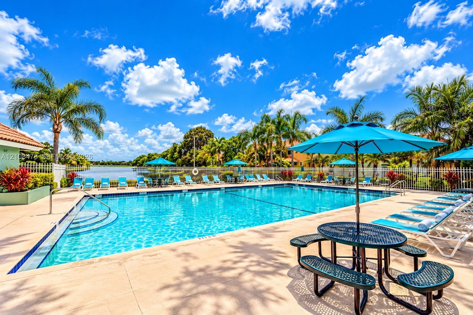 Rectangular swimming pool featuring a concrete deck, metal perimeter fencing, integrated entry steps, and a waterfront setting with mature palm trees