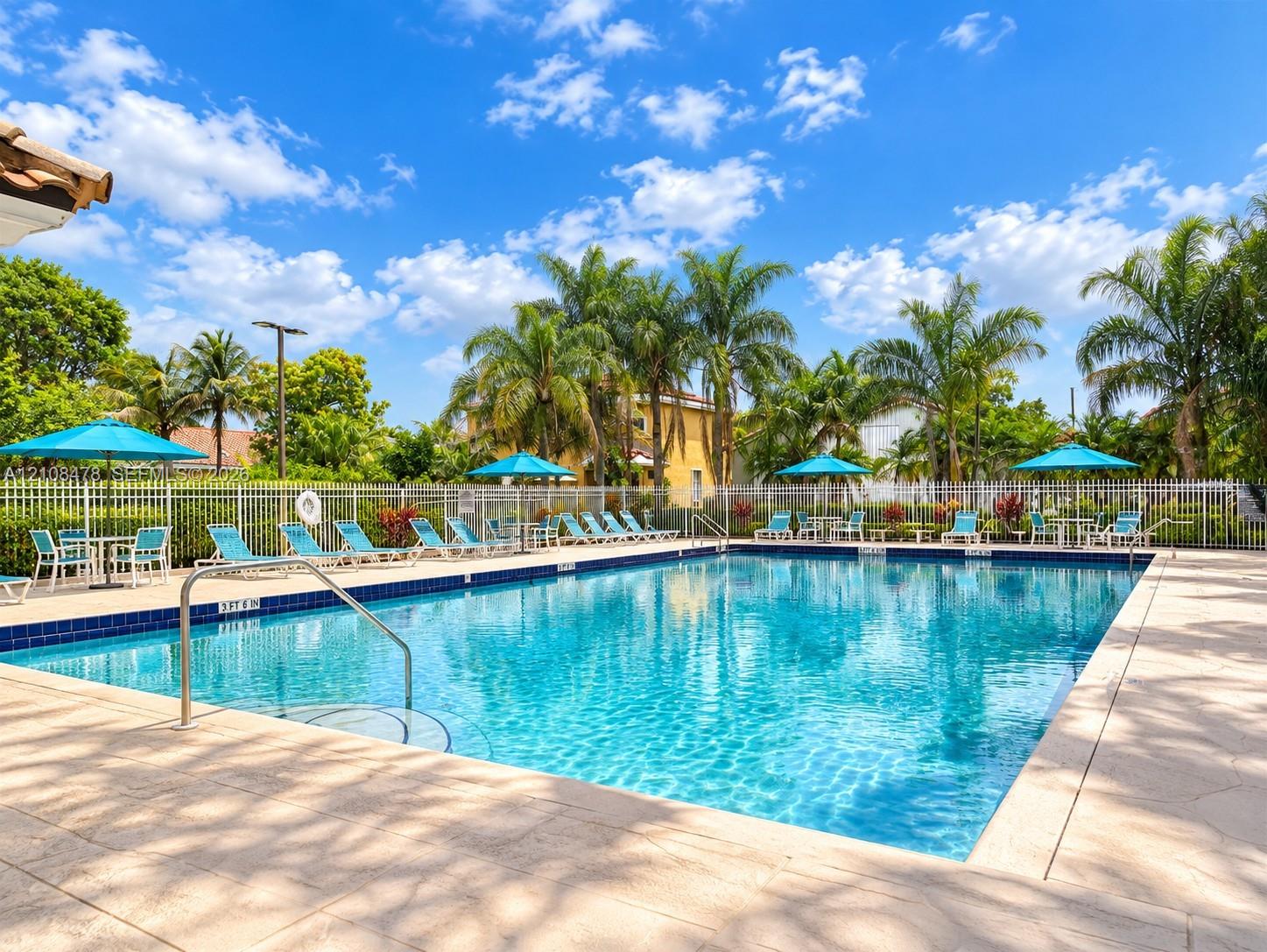 Swimming pool with a paved deck, metal perimeter fencing, and mature palm trees