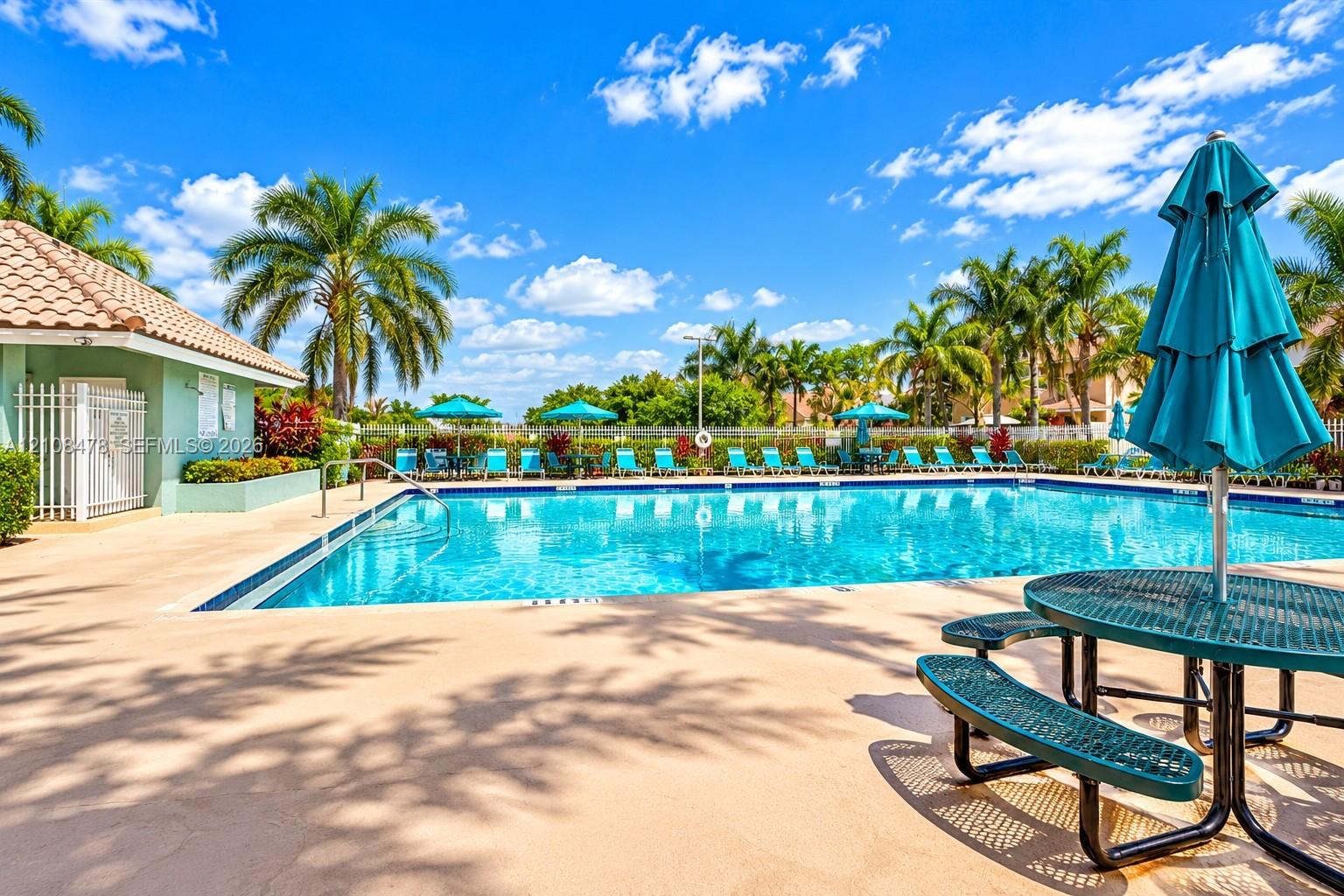 Outdoor swimming pool featuring a tiled deck, perimeter landscaping, and a pool house with a tile roof