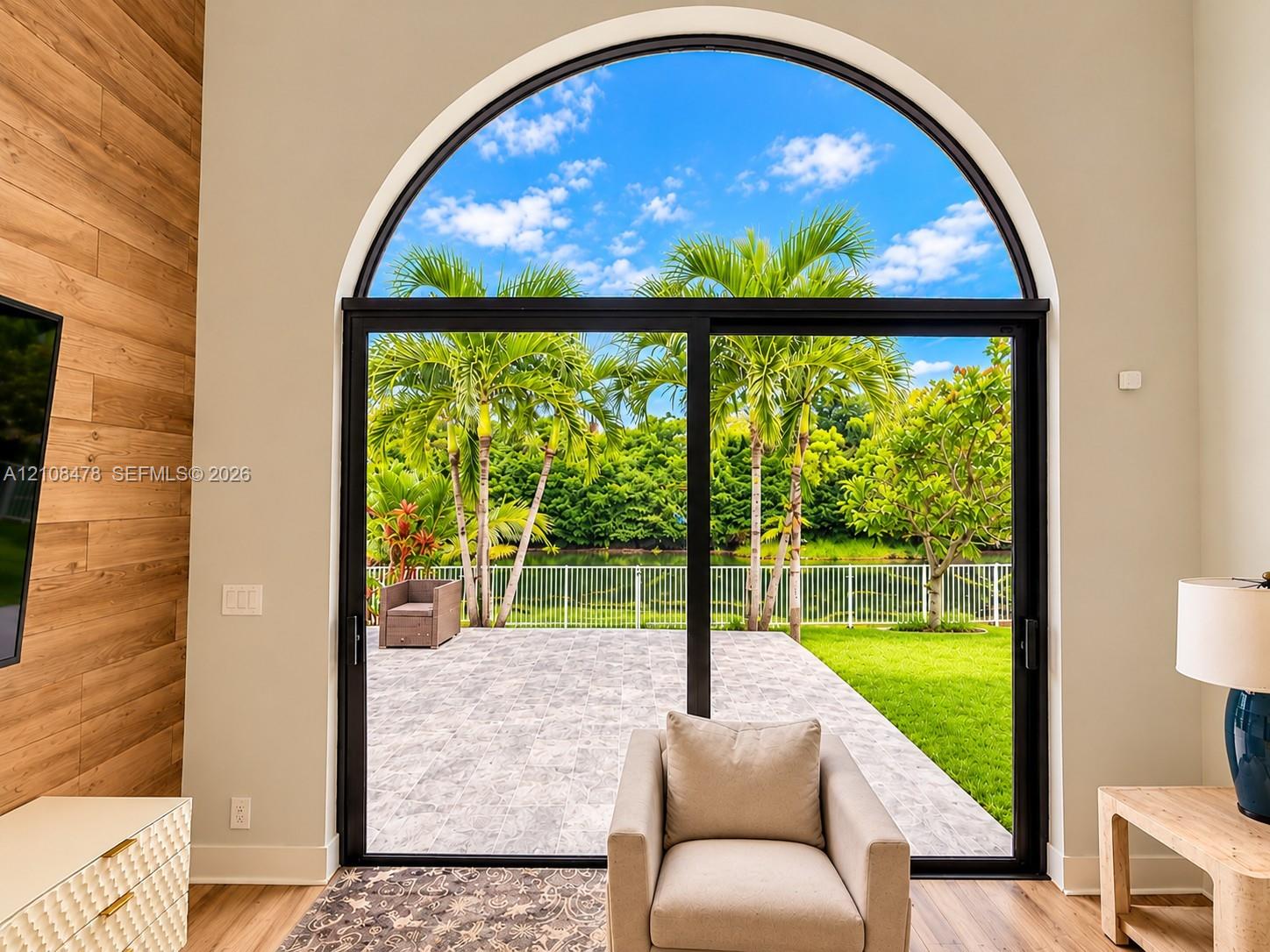 Arched floor-to-ceiling glass panel, horizontal wood-plank accent wall, and stone-paver outdoor patio