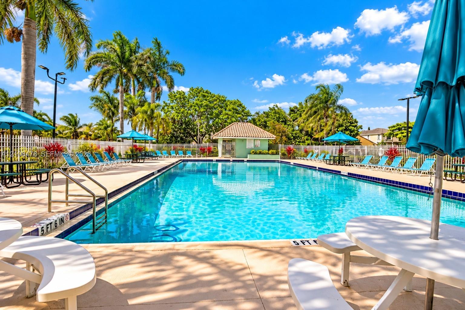 Swimming pool featuring a tiled perimeter, metal entry handrails, surrounding paved decking, and a dedicated pool house structure