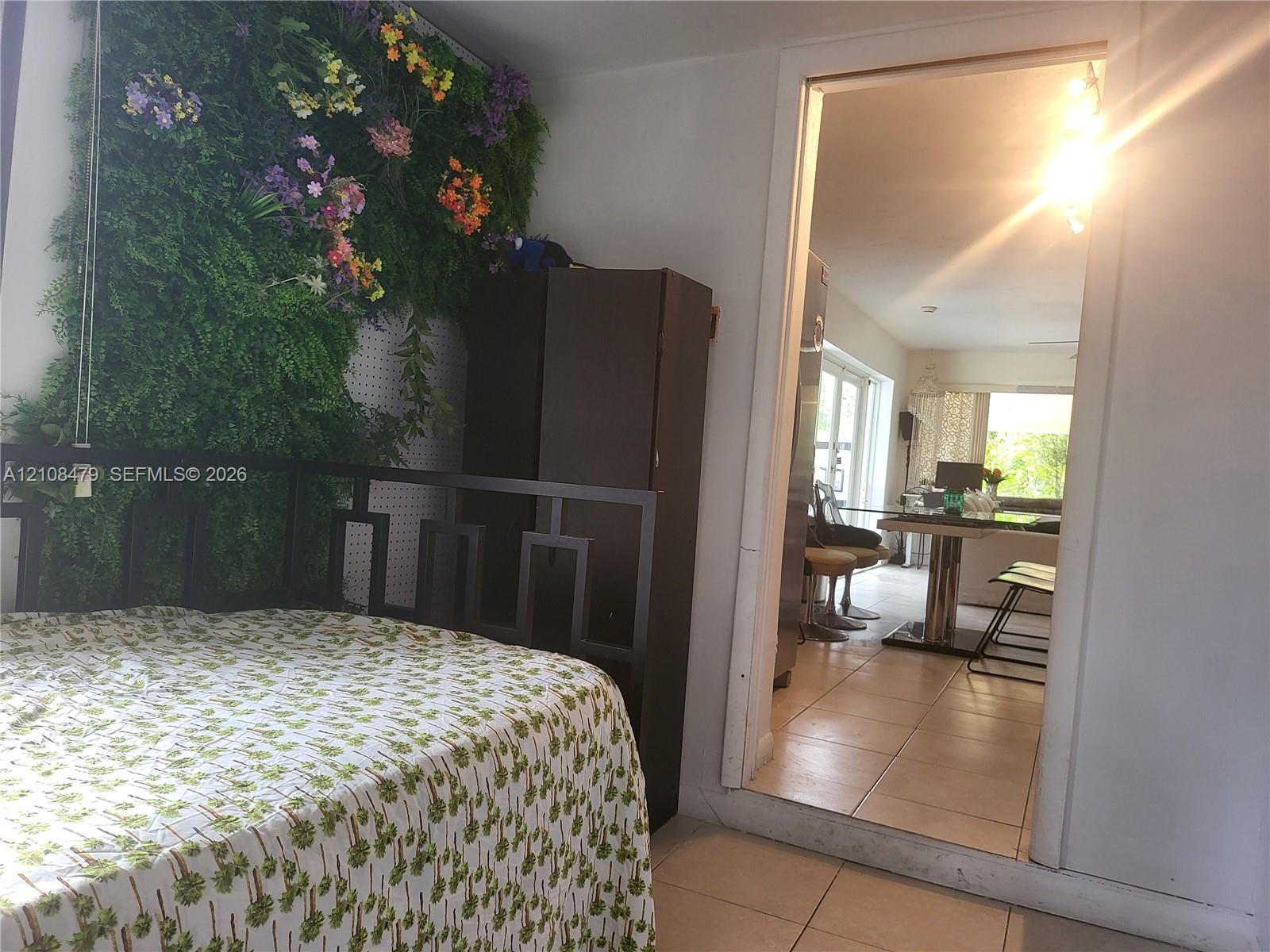 Room featuring large-format neutral floor tiling, a decorative wall-mounted botanical installation, and a doorway leading to a secondary space with a window