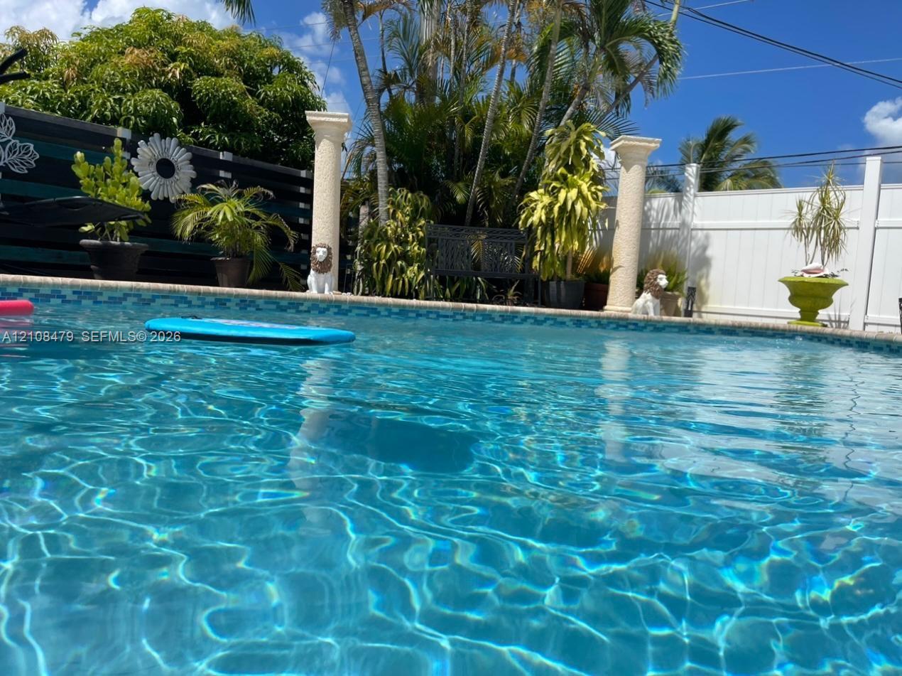 In-ground swimming pool featuring tiled coping, flanked by decorative architectural columns and enclosed by solid perimeter fencing