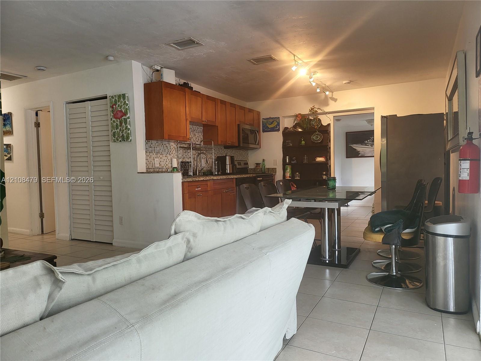 Kitchen featuring wood cabinetry, stone countertops, mosaic tile backsplash, stainless steel appliances, and tile flooring
