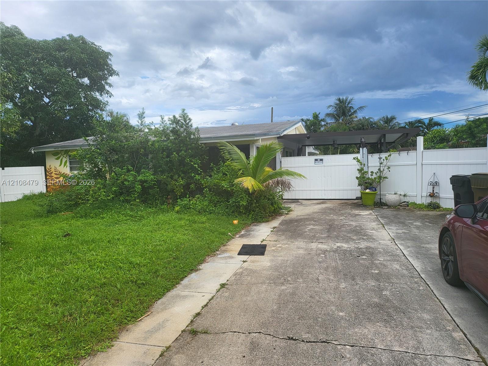 Single-story residence featuring a concrete driveway, attached carport, and full-perimeter white vinyl fencing