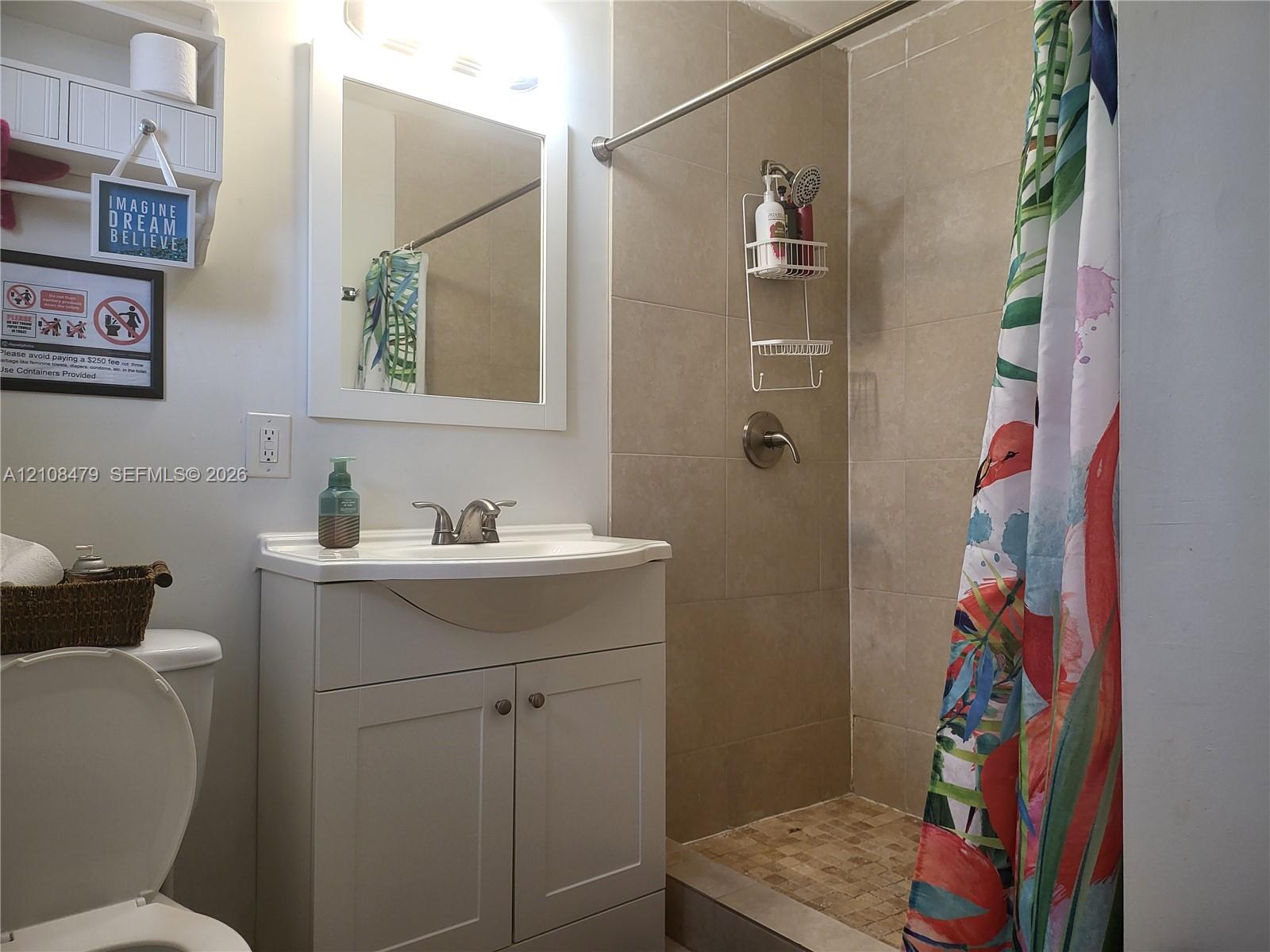 Bathroom featuring a white vanity cabinet with an integrated basin, wall-mounted mirror, built-in shelving unit, and a tiled shower enclosure