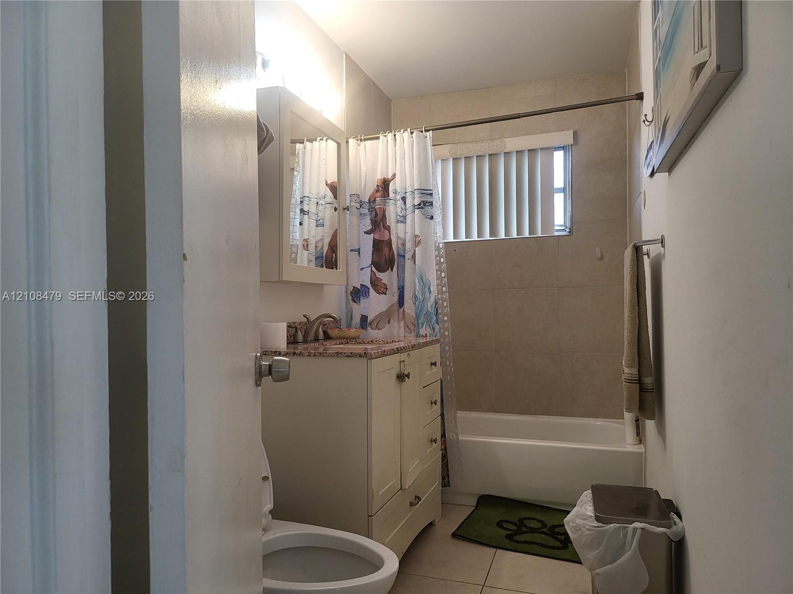 Bathroom featuring a vanity with stone-finish countertop, integrated sink, built-in medicine cabinet, ceramic tile tub surround, and vertical blind window covering