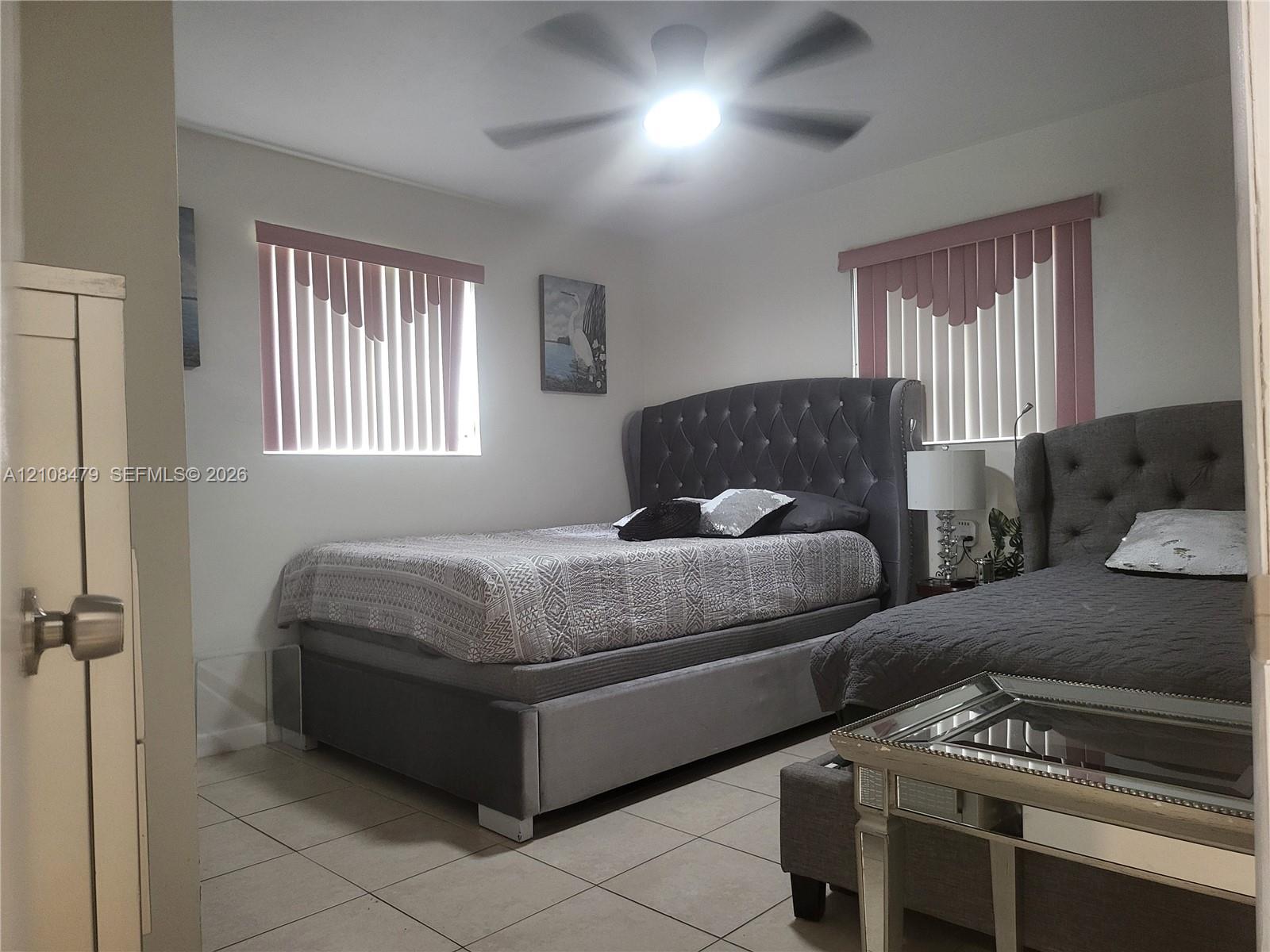 Neutral-toned tile flooring, dual windows, and an integrated ceiling fan with light fixture