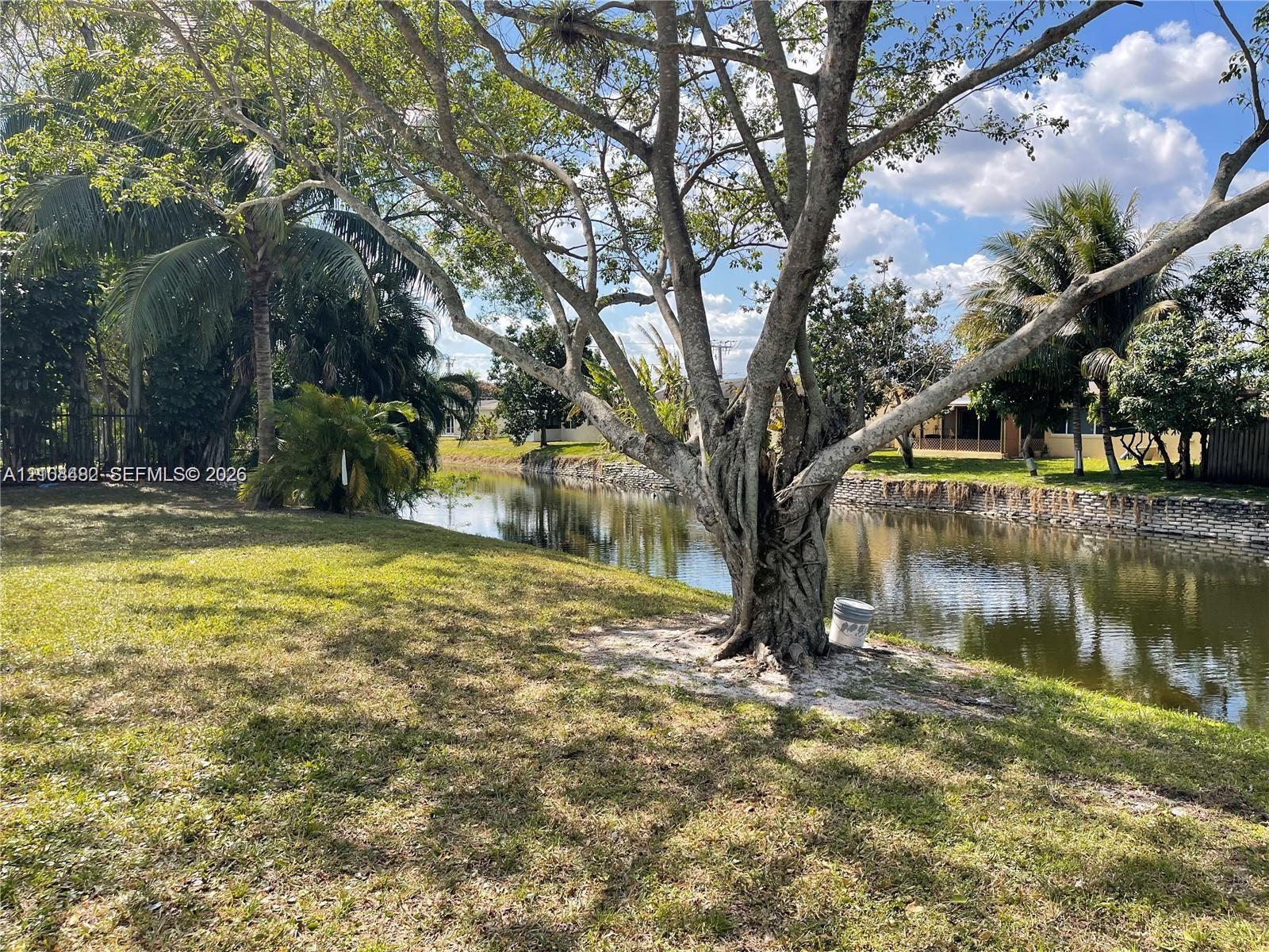 Waterfront backyard featuring mature trees, a manicured lawn, and a stone-lined canal bulkhead Waterfront backyard featuring mature trees, a manicured lawn, and a stone-lined canal bulkhead