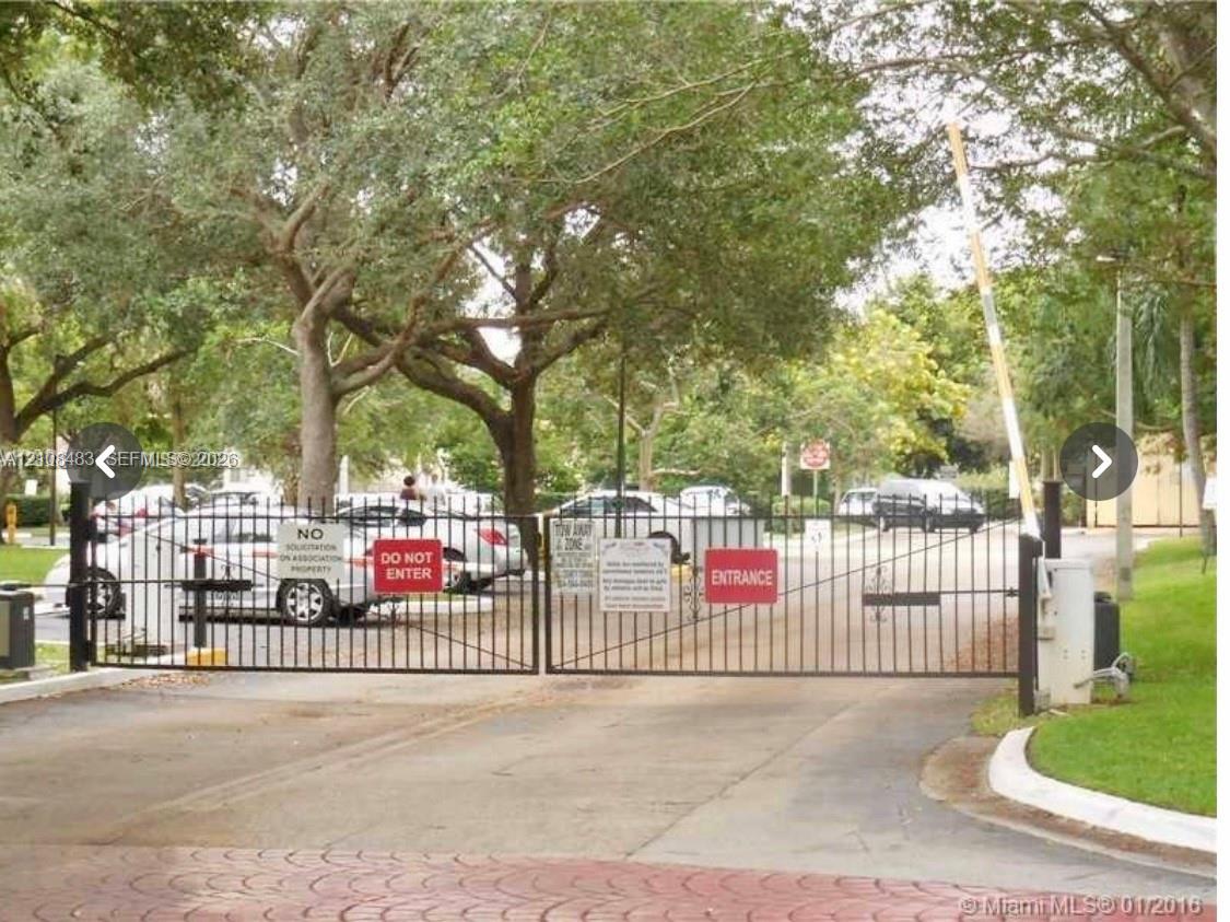 Gated entry featuring a metal vehicle barrier and mature perimeter trees