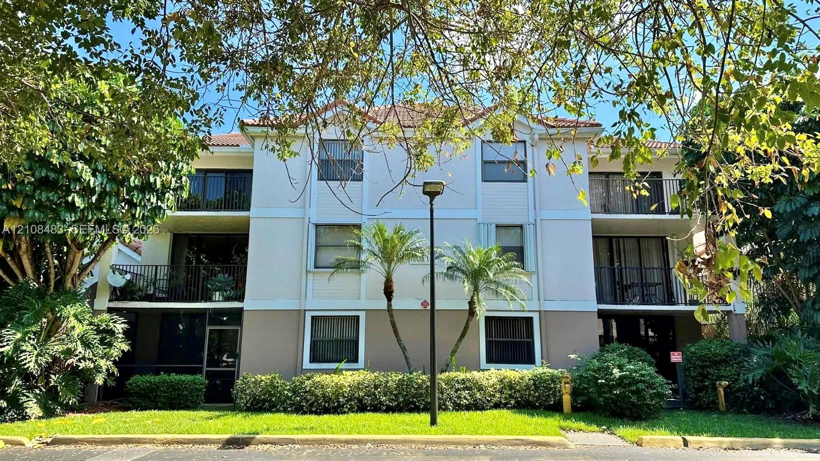 Three-story multi-unit structure featuring a stucco exterior, integrated private balconies, tile roofing, and mature landscaping