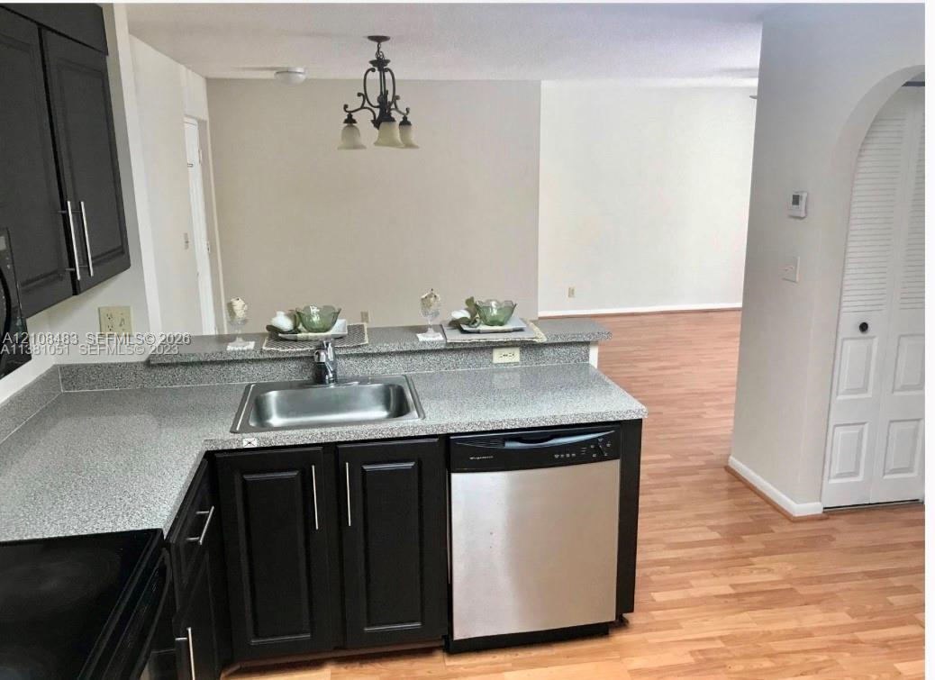 Kitchen featuring dark cabinetry, stone-finish countertops, stainless steel undermount sink, built-in dishwasher, and wood-finish flooring