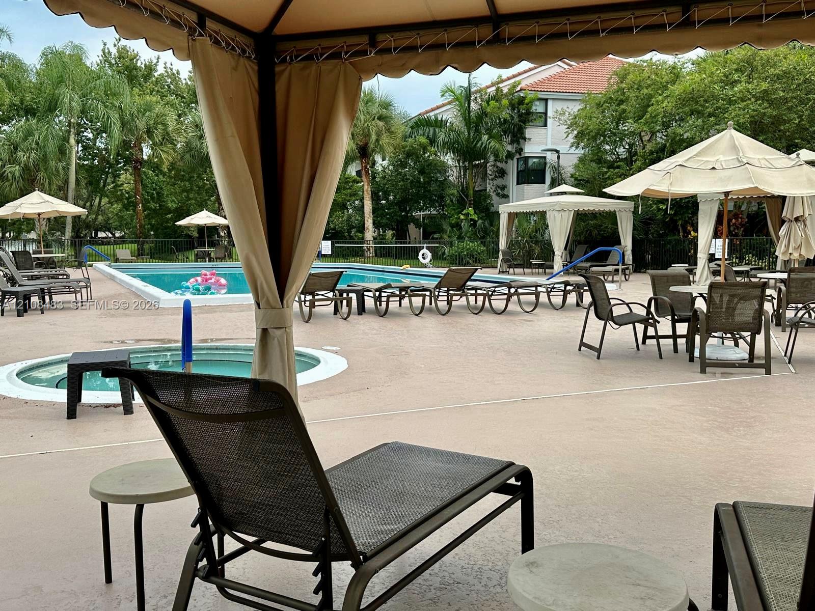 Community swimming pool with an integrated spa, concrete deck, and multiple shaded gazebo structures