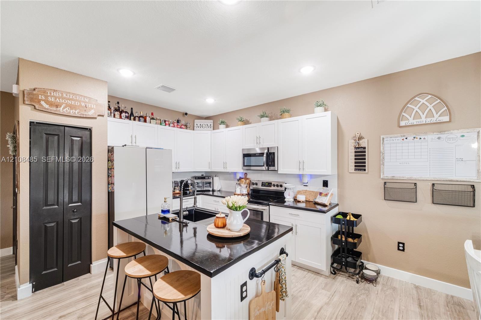 Kitchen featuring white shaker-style cabinetry, an island with a stone-surface countertop, wood-finish flooring, recessed lighting, and an integrated microwave